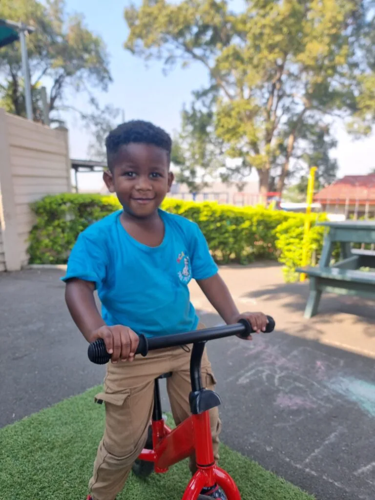 Confident preschooler riding a bicycle with training wheels at Scamps Pre Primary Queensburgh