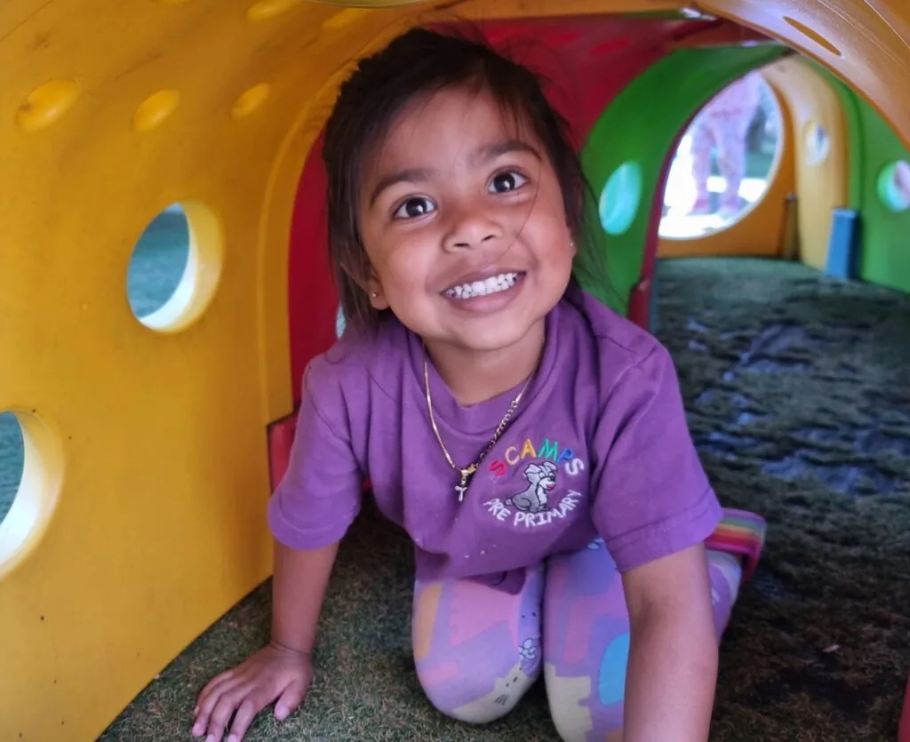 A happy Scamps child laughing while crawling through the colourful play tunnel